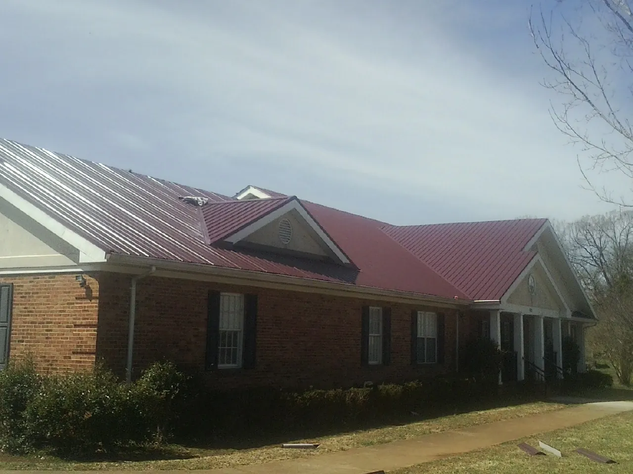 Red metal roof with gabled entries on a long brick building, from a Hail Damage Roof Repair job in Godwin