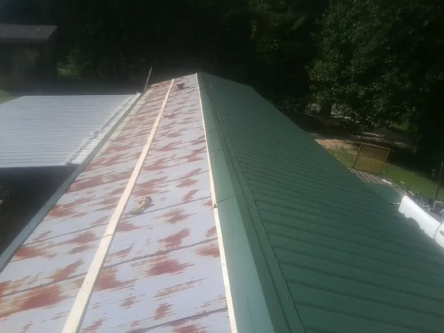 Old rusted panels beside newly installed green metal roofing — Wind Damage Roof Repair by Roofing Brothers in Godwin